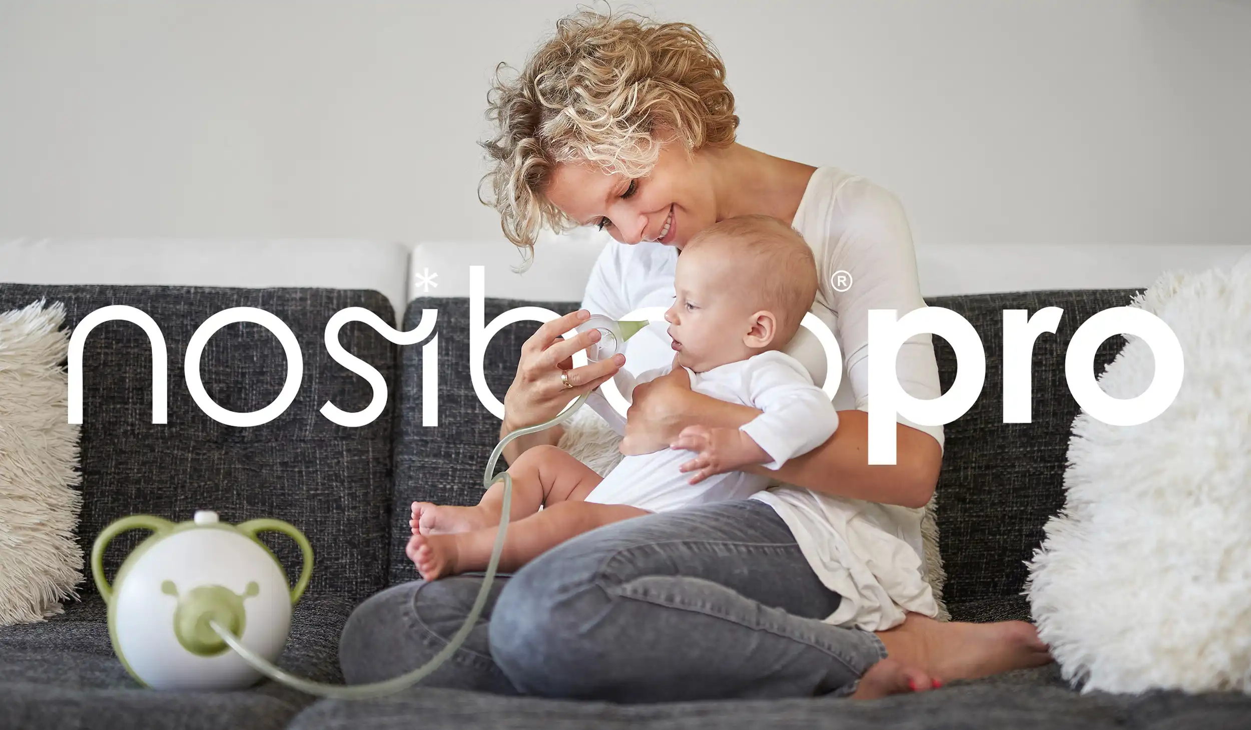 Mama używa aspiratora Nosiboo Pro w wersji Sage Green, trzymając niemowlę na kolanach – bezpieczne i delikatne oczyszczanie nosa