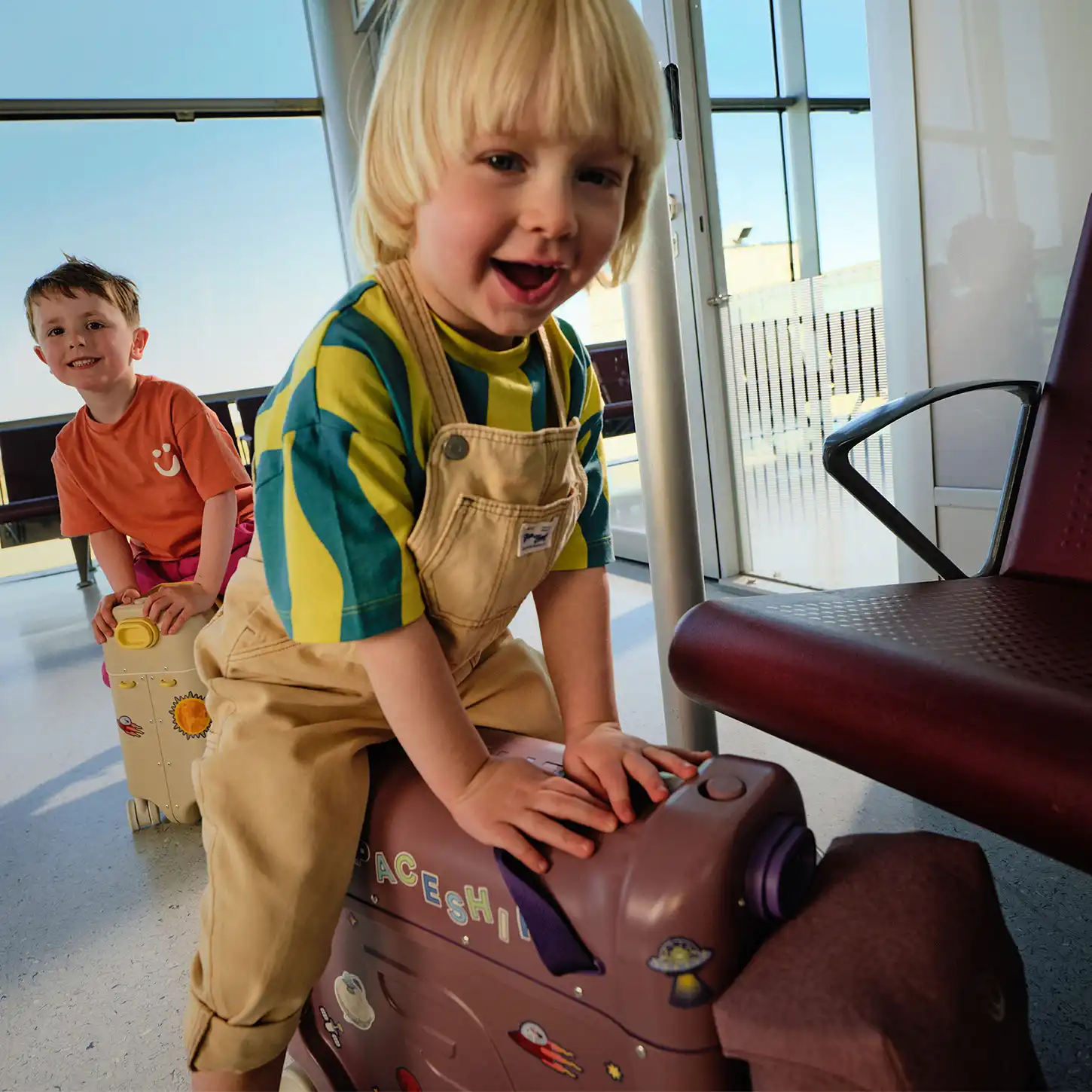 Dzieci bawiące się walizkami JetKids BedBox na lotnisku – walizka służąca jako jeździk w czasie oczekiwania na podróż
